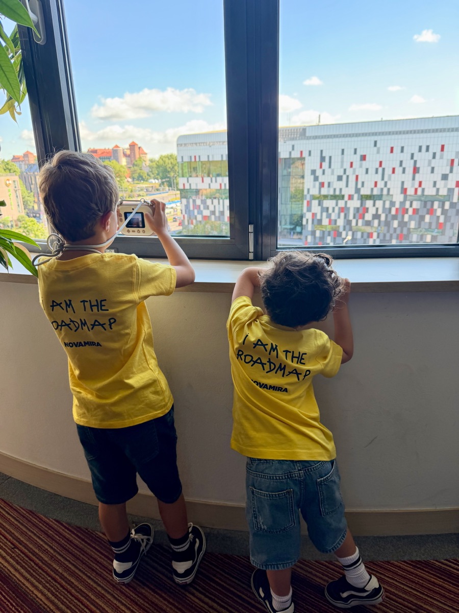 Two kids in Novamira I am the roadmap t-shirts looking out of a window